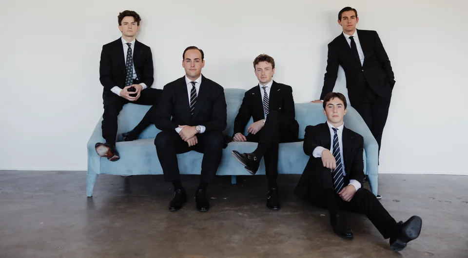 A seated group composition in dark suits on a blue couch.