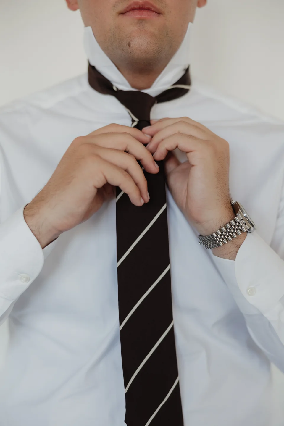 Adjusting a striped tie over a white shirt.