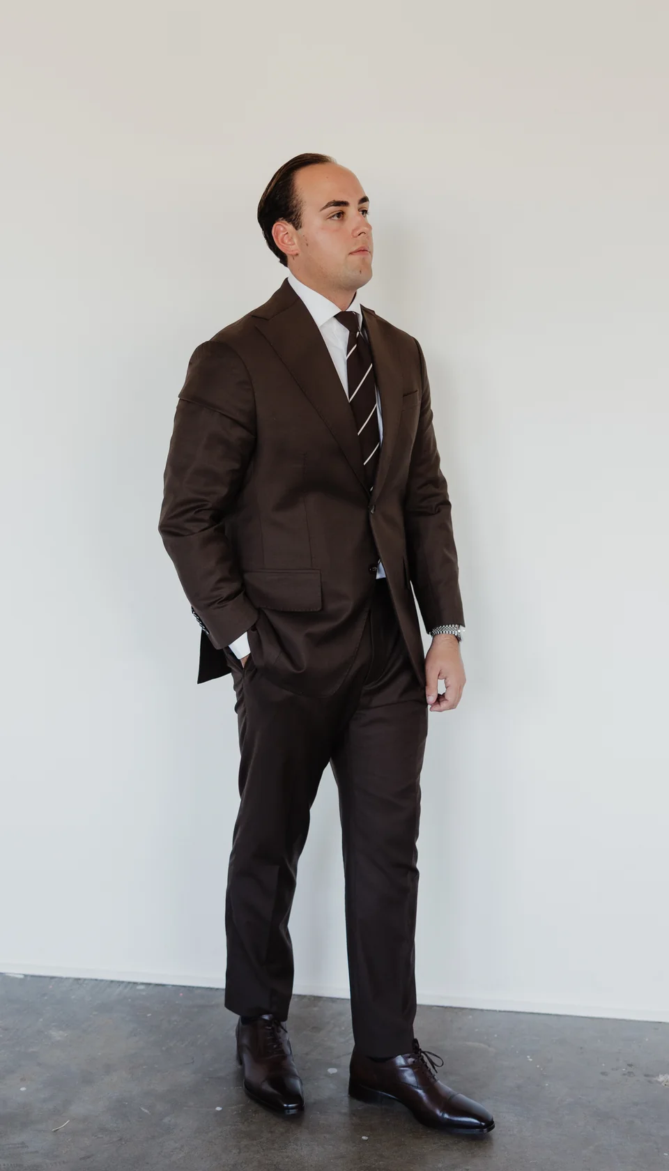 Full-length brown suit with a striped tie.
