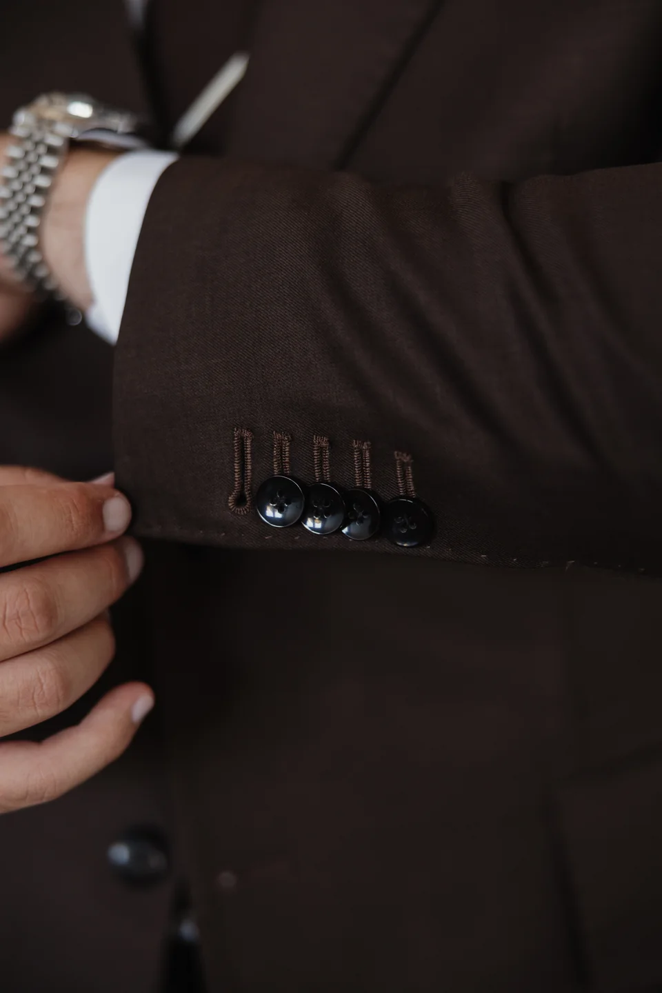 Brown suit sleeve, buttons and wristwatch detail.